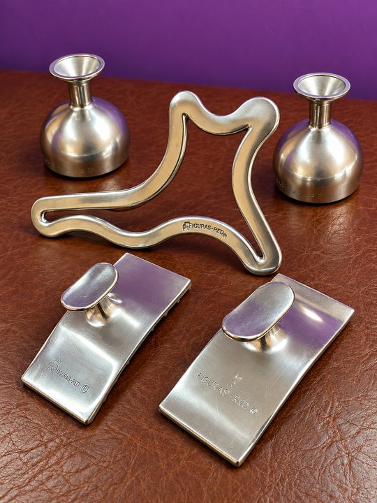 Las piezas de metaloterapia de Flor: dos copas, un contorno y dos placas de metal sobre la camilla